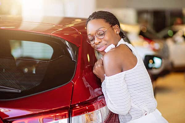 Happy African American woman hugging a car.